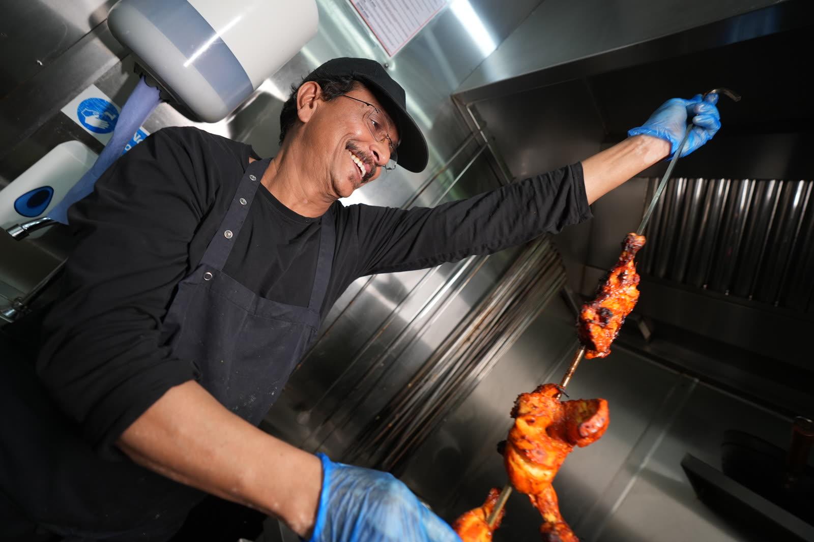 A chef pulling skewers from the clay tandoor as flame licks up around them