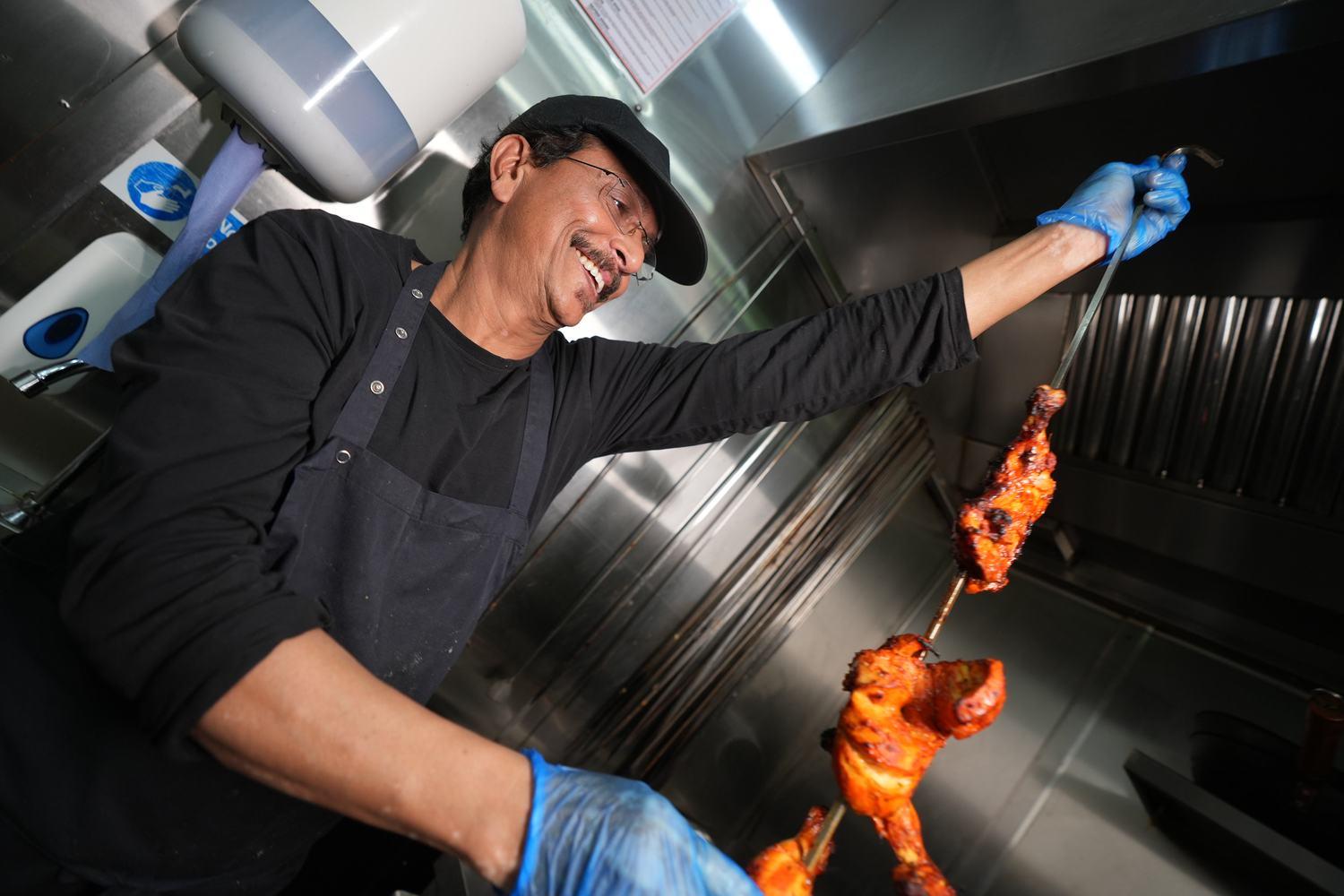 A chef lifting skewers of tandoori chicken from the clay tandoor
